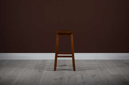 Stylish wooden stool near brown wall indoorsの写真素材