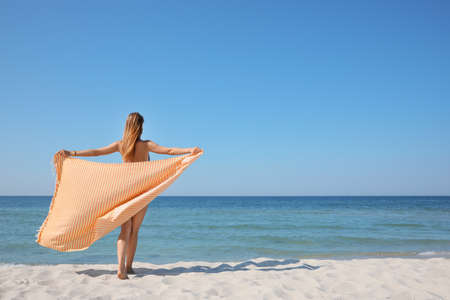 Woman with beach towel near sea on sunny day, back viewの写真素材
