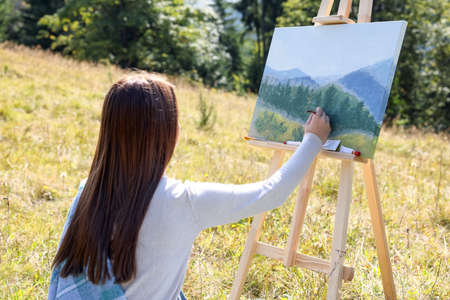 Young woman drawing on easel outdoors, back viewの写真素材