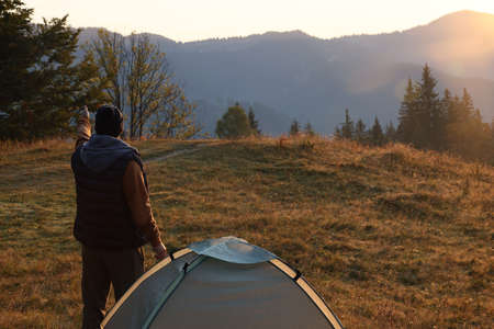 Tourist enjoying sunrise near camping tent in mountains, back viewの写真素材