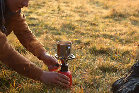 Tourist making hot drink with camping burner outdoors, closeup. Space for textの写真素材