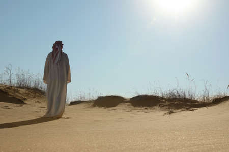 Man in arabic clothes walking through desert on sunny day, back viewの写真素材