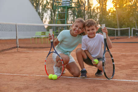 Cute children with tennis rackets and balls on court outdoorsの写真素材
