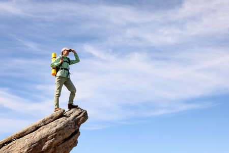 Young woman with backpack on rocky peak in mountains. Space for textの写真素材