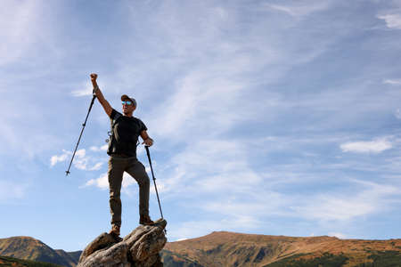 Man with backpack and trekking poles on rocky peak in mountainsの写真素材