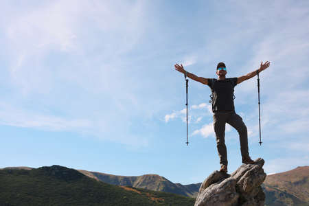 Man with backpack and trekking poles on rocky peak in mountainsの写真素材