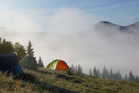 Picturesque foggy mountain landscape with camping tents in morning. Space for textの写真素材
