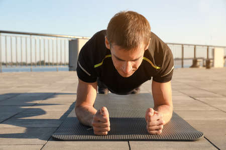 Sporty man doing plank exercise on mat outdoorsの写真素材