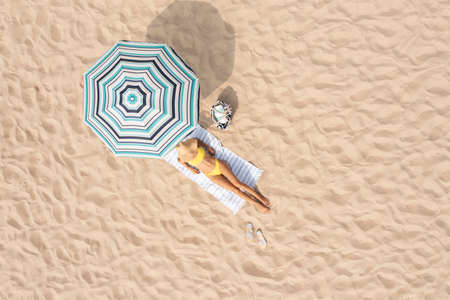 Woman resting under striped beach umbrella at sandy coast, aerial view. Space for textの写真素材
