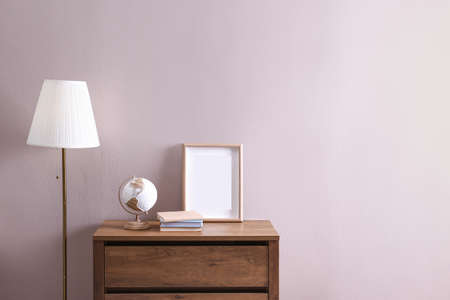 Wooden chest of drawers with globe, books and empty frame near beige wall in room, space for text. Interior designの写真素材