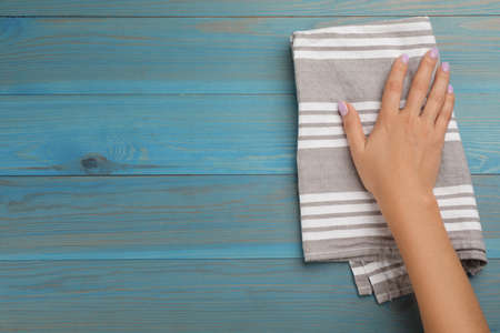 Woman wiping light blue wooden table with kitchen towel, top view. Space for textの写真素材