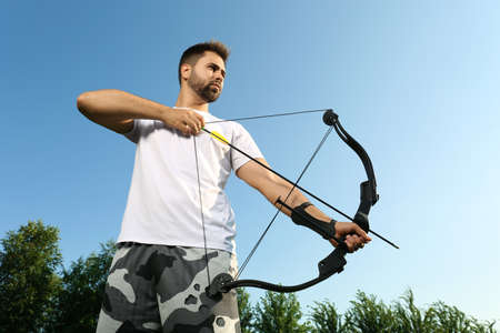 Man with bow and arrow practicing archery outdoors, low angle viewの写真素材