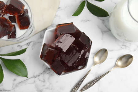 Delicious grass jelly cubes, milk and green leaves on white marble table, flat layの写真素材