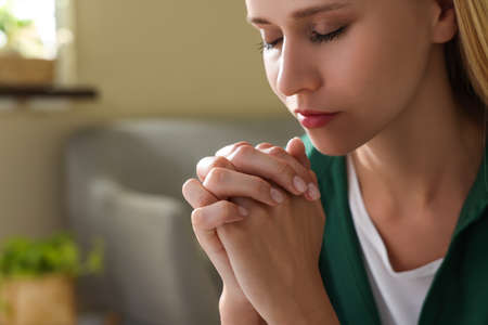 Religious young woman with clasped hands praying indoors, closeup. Space for textの写真素材