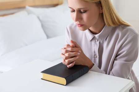 Religious young woman with Bible praying in bedroomの写真素材