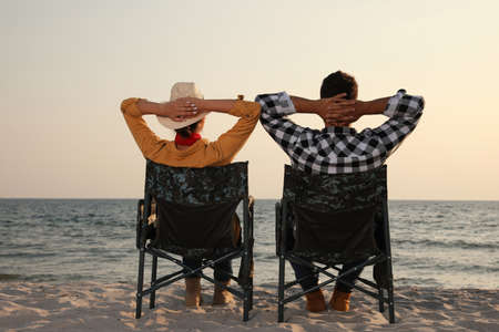 Couple sitting in camping chairs and enjoying seascape on beach, back viewの写真素材