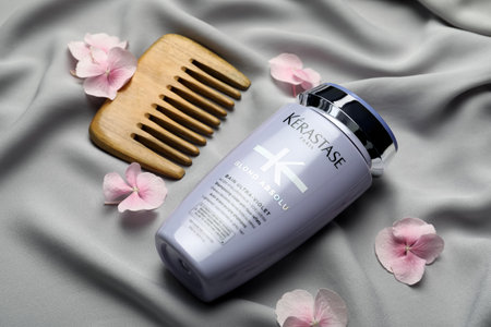 MYKOLAIV, UKRAINE - SEPTEMBER 07, 2021: Kerastase shampoo, hair comb and hydrangea florets on gray fabricのeditorial素材