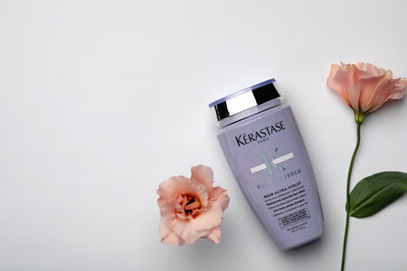 MYKOLAIV, UKRAINE - SEPTEMBER 07, 2021: Kerastase shampoo and beautiful flowers on light gray background, flat lay. Space for textのeditorial素材