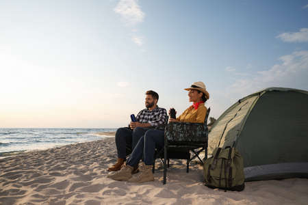 Couple with thermoses near camping tent on beachの写真素材