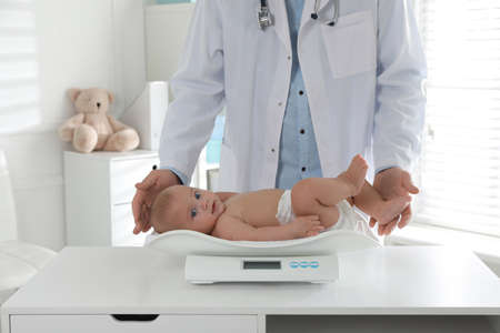 Pediatrician weighting cute baby in clinic, closeup. Health careの写真素材