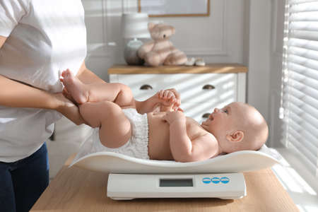 Young woman weighting her cute baby at home, closeup. Health careの写真素材