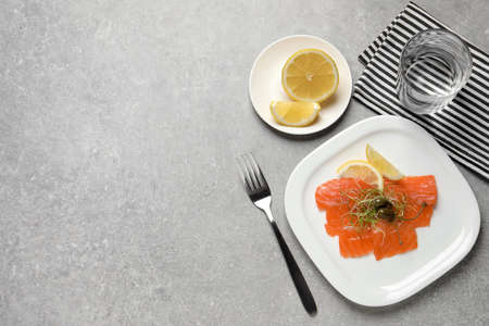 Salmon carpaccio with capers, microgreens and lemon served on grey table, flat lay. Space for textの写真素材