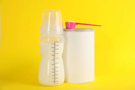 Blank can of powdered infant formula with feeding bottle and scoop on yellow background. Baby milkの写真素材