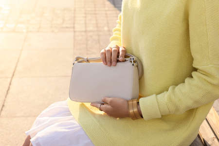 Fashionable woman with stylish bag on bench outdoors, closeupの写真素材