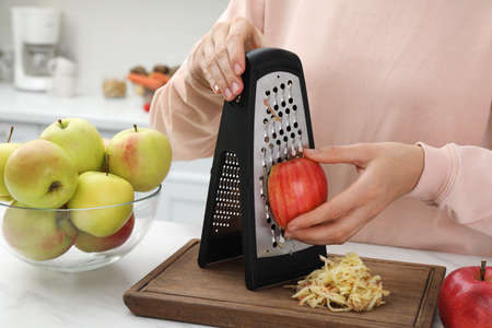 Woman grating fresh red apple at kitchen table, closeupの写真素材