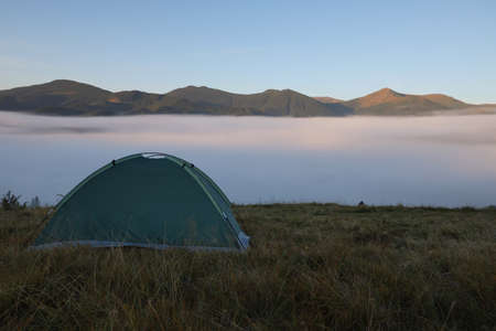 Picturesque mountain landscape with camping tent in foggy morning. Space for textの写真素材