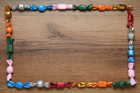 Frame of candies in colorful wrappers on wooden table, flat lay. Space for textの写真素材