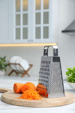 Grater and fresh ripe carrot on white table in kitchen. Space for textの写真素材