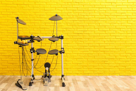 Modern electronic drum kit near yellow brick wall indoors, space for text. Musical instrumentの写真素材