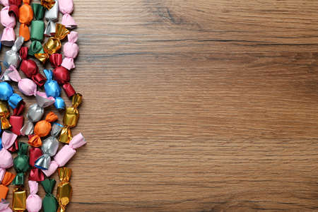 Many candies in colorful wrappers on wooden table, flat lay. Space for textの写真素材