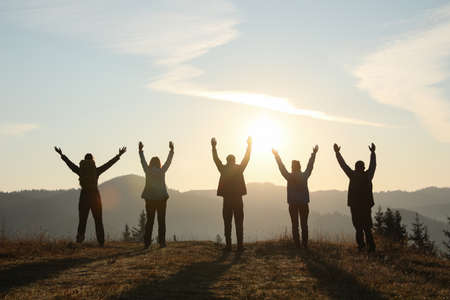Group of people enjoying sunrise in mountains, back viewの写真素材