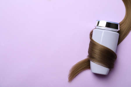 Bottle wrapped in lock of hair on violet background, top view with space for text. Natural cosmetic productの写真素材