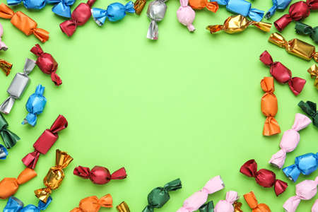 Frame of candies in colorful wrappers on light green background, flat lay. Space for textの写真素材