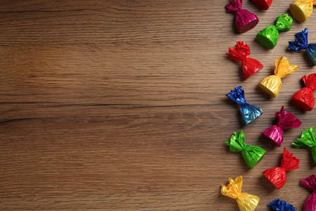 Many candies in colorful wrappers on wooden table, flat lay. Space for textの写真素材
