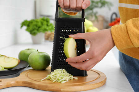 Woman grating fresh green apple at kitchen counter, closeupの写真素材