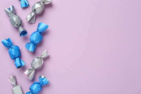Many candies in light blue and silver wrappers on violet background, flat lay. Space for textの写真素材