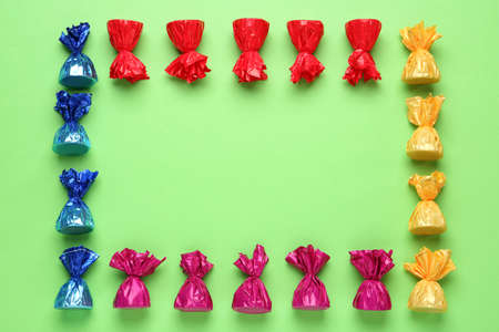 Frame of candies in colorful wrappers on light green background, flat lay. Space for textの写真素材