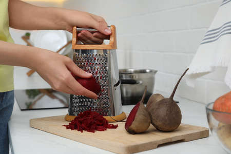 Woman grating fresh beetroot at kitchen counter, closeupの写真素材