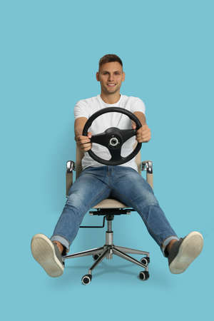 Happy man on chair with steering wheel against light blue backgroundの写真素材
