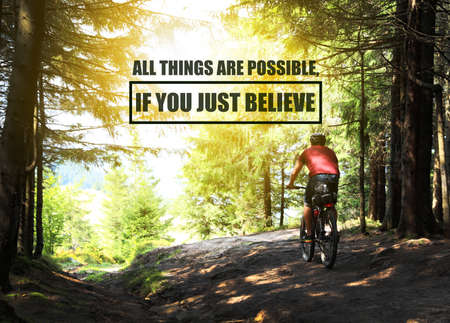 All Things Are Possible, If You Just Believe. Inspirational quote saying about power of faith. Text against view of cyclist riding bike down beautiful forest trailの写真素材