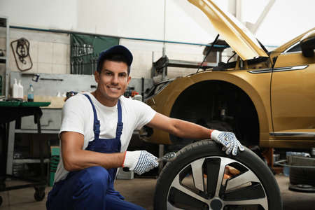 Portrait of professional mechanic with car wheel at automobile repair shopの写真素材