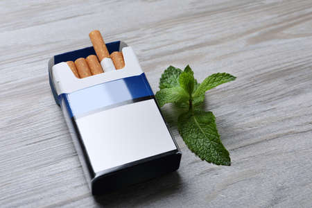 Pack of menthol cigarettes and mint on light wooden tableの写真素材