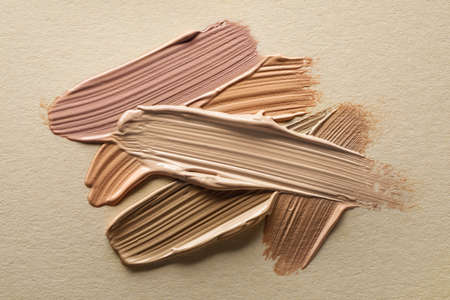 Different shades of liquid foundation on beige background, top view