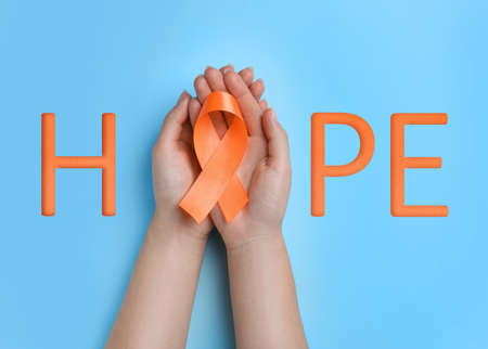 Word HOPE and woman with orange awareness ribbon on light blue background, top viewの写真素材