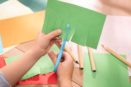 Little boy cutting color paper with scissors at table indoors, closeupの写真素材