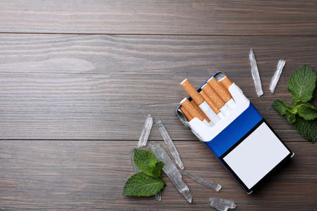 Pack of cigarettes, menthol crystals and mint on wooden table, flat lay. Space for textの写真素材
